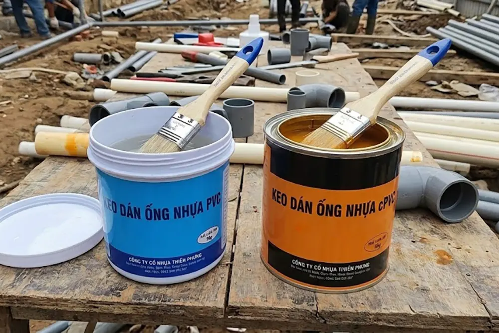 Hai hộp keo dán ống nhựa, một màu trong dùng cho PVC và một màu vàng cam dùng cho cPVC